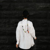 Person wearing a white shirt and dark pants against a black textured wall.