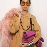 Person wearing a beige trench coat with a pink fur stole and holding a pink bag against a white background