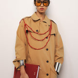 Person wearing a beige trench coat with a red book and decorative strings against a white background