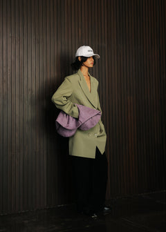 Person wearing a green coat and white cap against a dark wooden wall