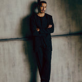 Man in a black suit standing against a textured wall with 'BAZAAR' logo.